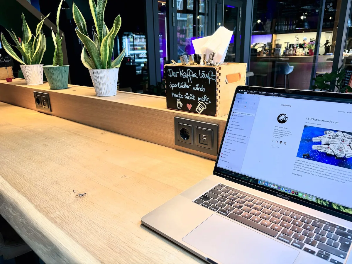 Ein Laptop auf einem Holztisch mit Pflanzen im Hintergrund.