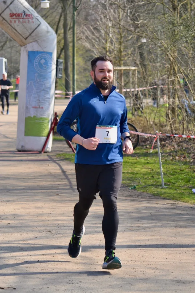 Ein Mann im dunkelblauen Laufschirt und langer Laufhose läuft durch den Park